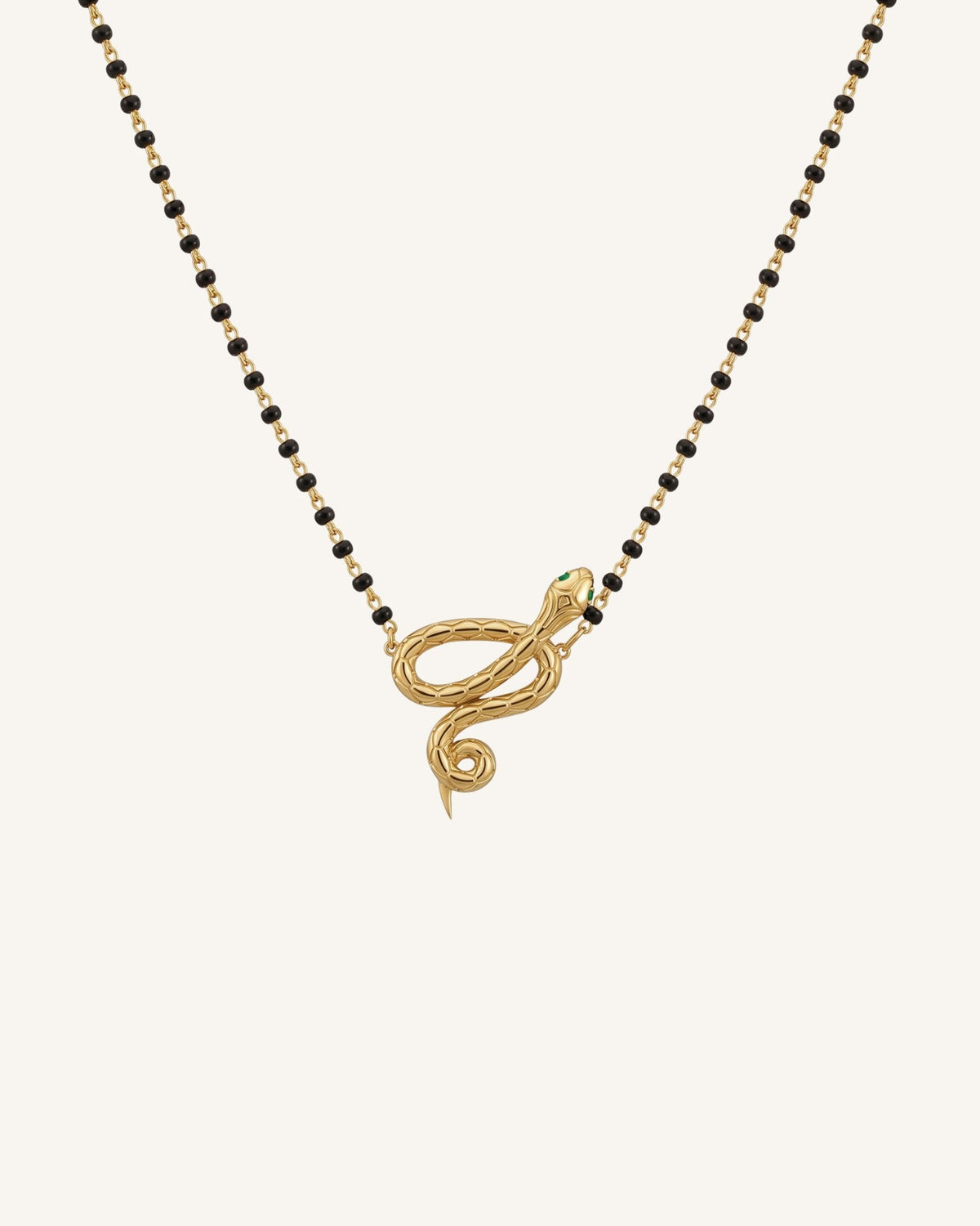 The Ammama 18K gold twin serpent necklace with emerald eyes on a black-beaded chain