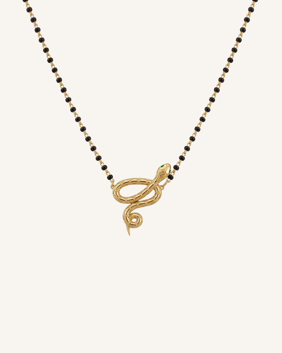 The Ammama 18K gold twin serpent necklace with emerald eyes on a black-beaded chain