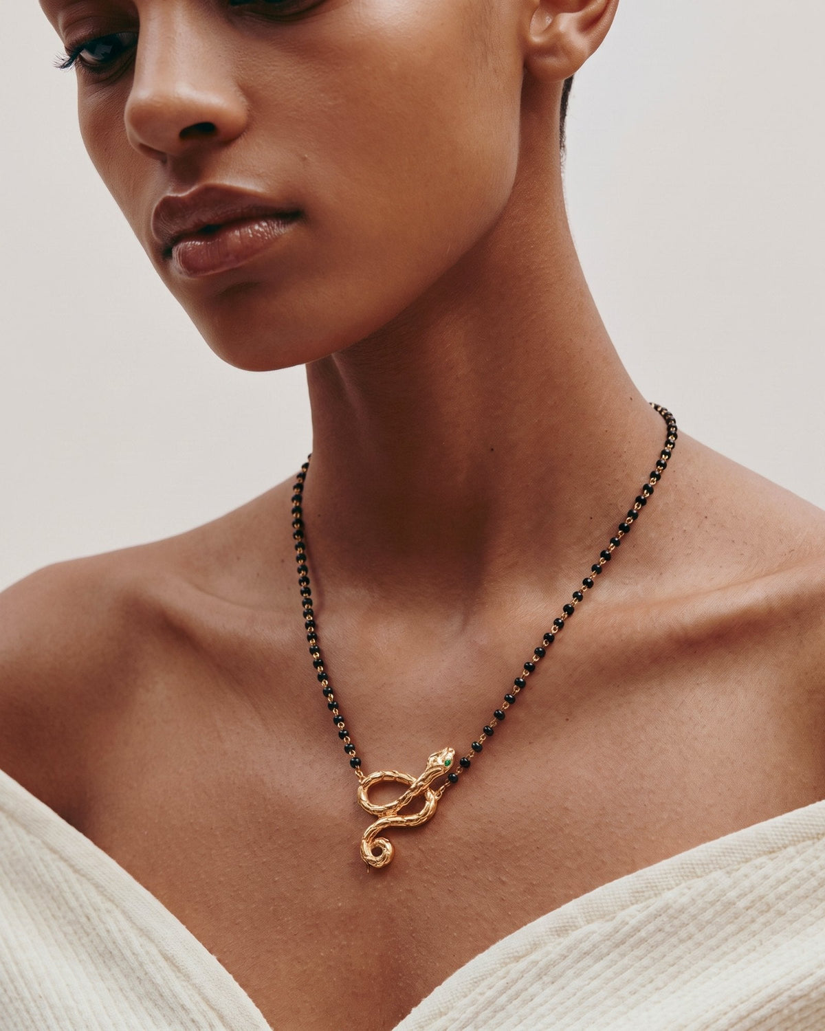 The Ammama 18K gold twin serpent necklace with emerald eyes on a black-beaded chain
