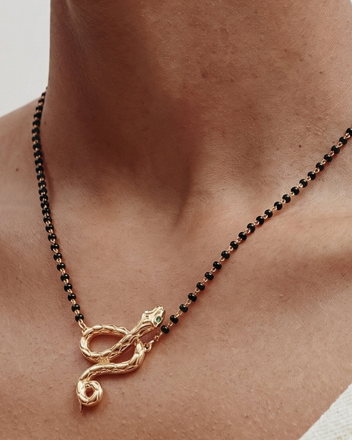 The Ammama 18K gold twin serpent necklace with emerald eyes on a black-beaded chain